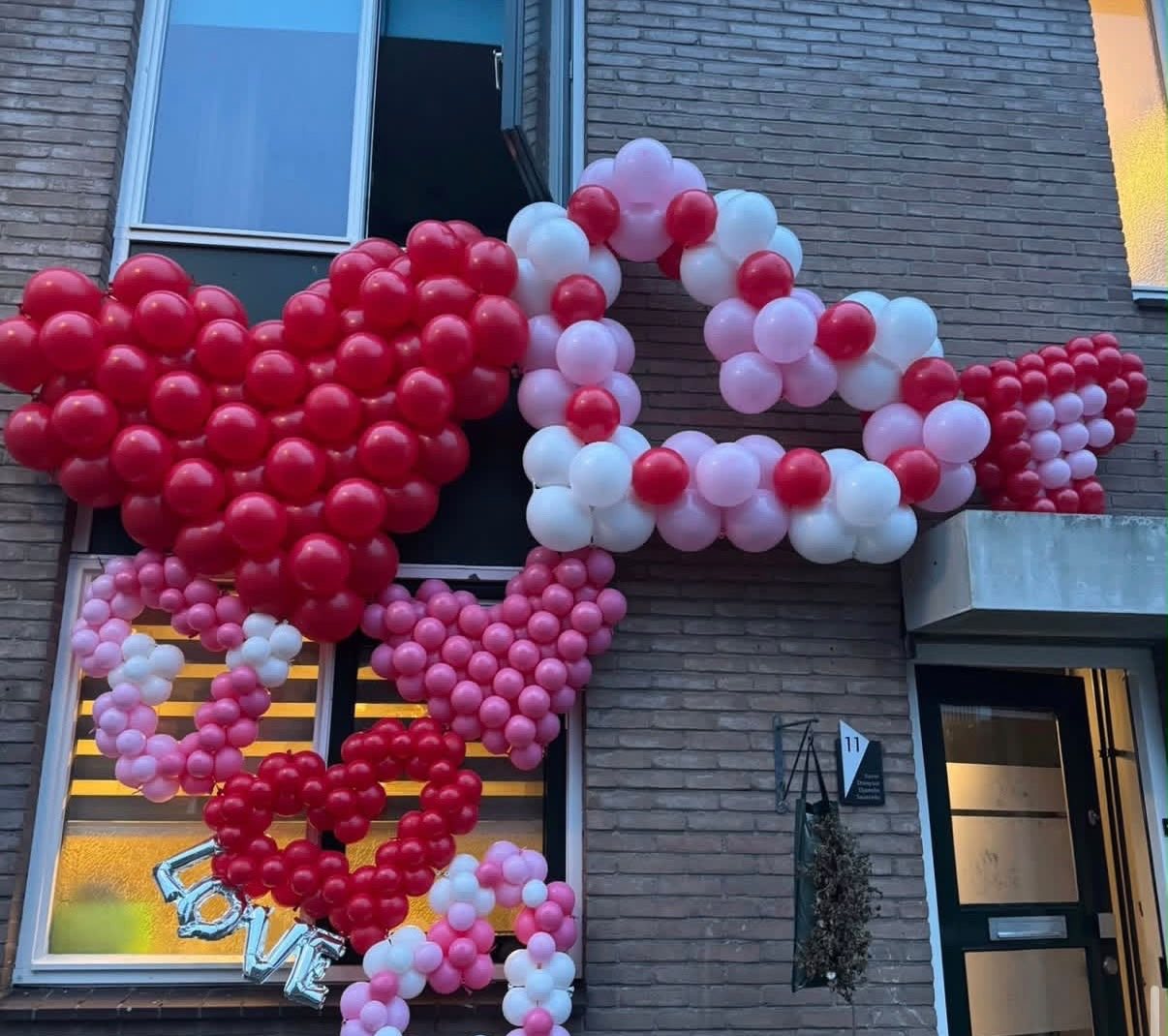 Ballonhartjes in rood, roze en wit tegen de gevel