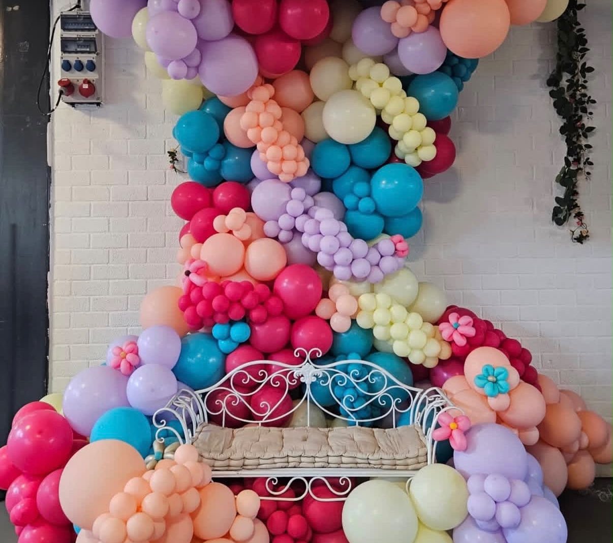 Kleurrijke organische ballonslinger in pasteltinten rond een wit bankje
